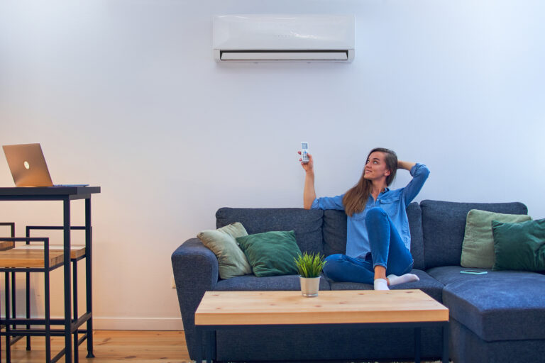 Young happy woman sitting on couch under air conditioner and adj